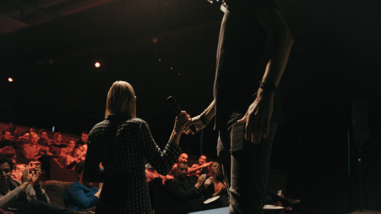 A woman onstage is handed the microphone to give her startup pitch.