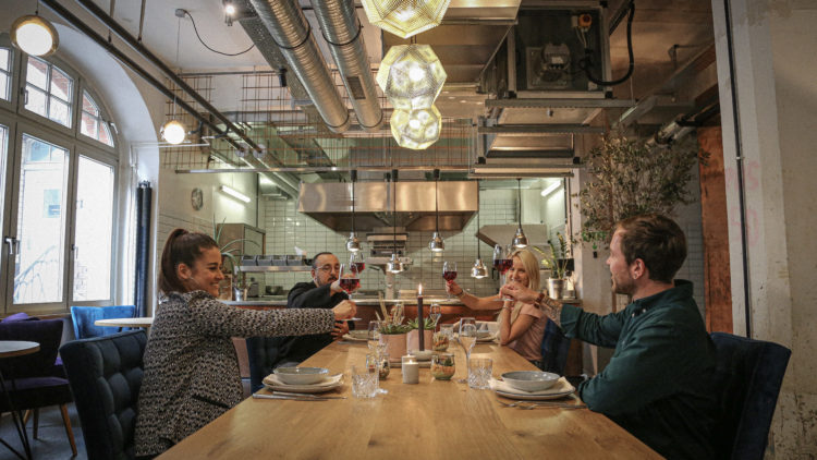 Guests to the Next Bite Show sit around the table with a glass of wine in conversation.