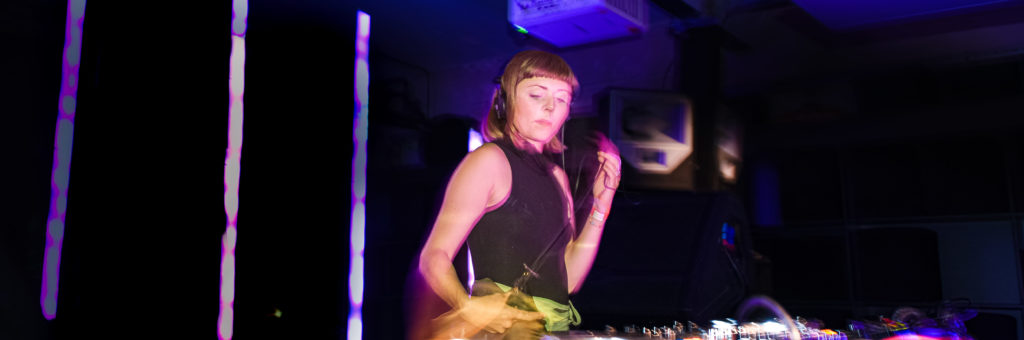 Woman in the foreground. Woman is dj-ing. The lighting is blue.