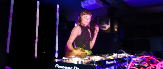 Woman in the foreground. Woman is dj-ing. The lighting is blue.