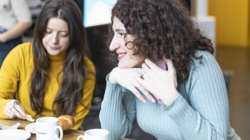 two women sitting on a table with cups and plates in front of them having breakfast